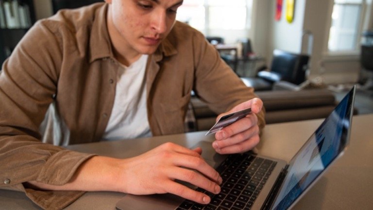Man holding a credit card while completing an online checkout on his laptop