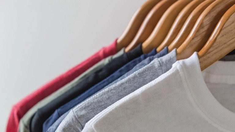 T-shirts in different colors hanging on wooden hangers, showing product color variations