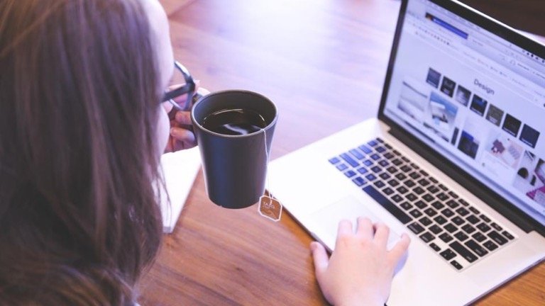 Woman browsing an online store product grid on a laptop while holding a coffee cup