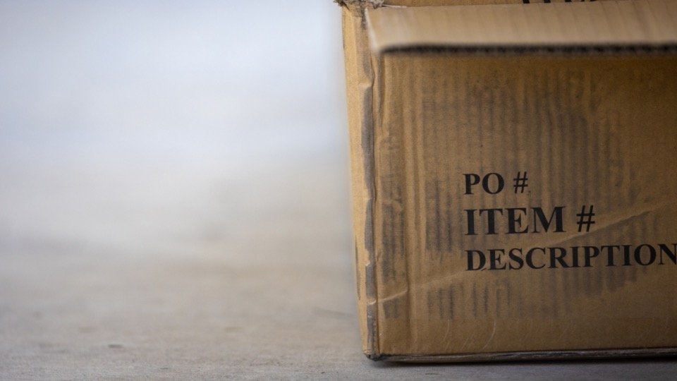 Cardboard shipping box with a PO number and item description label, ready for order tracking